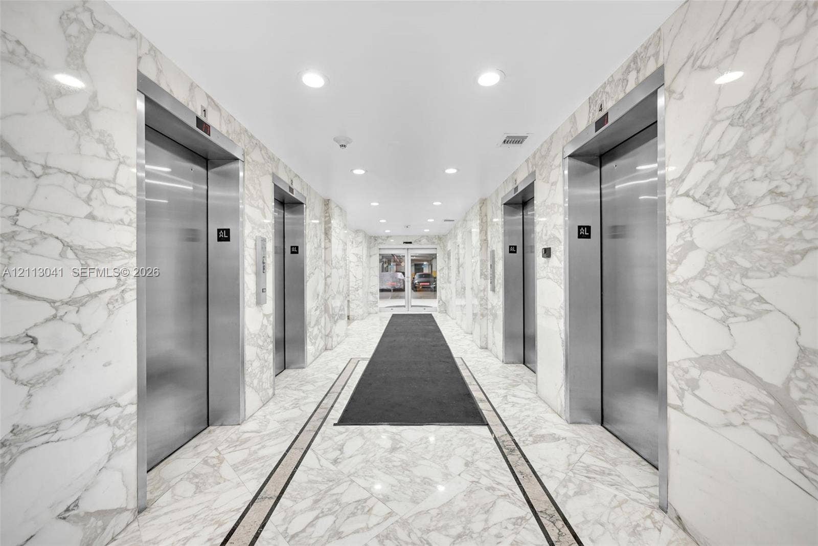 7135 Collins Avenue, #1426, Miami Beach, FL 33141 Elevator lobby featuring floor-to-ceiling stone wall cladding, polished stone flooring with decorative inlay, stainless steel elevator doors, and recessed ceiling lighting