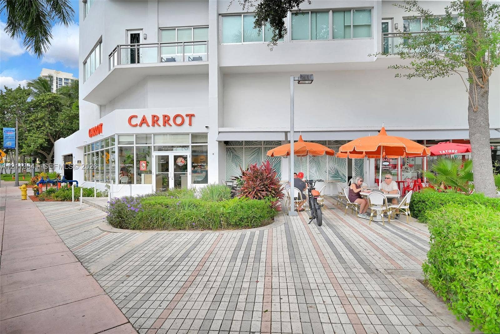 7135 Collins Avenue, #1426, Miami Beach, FL 33141 Multi-story commercial building exterior featuring expansive floor-to-ceiling storefront windows, integrated ground-level retail space, private balconies, and patterned paver hardscaping