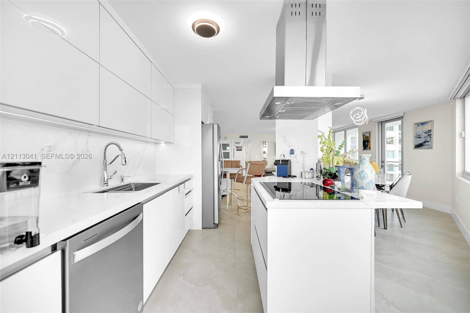 7135 Collins Avenue, #1426, Miami Beach, FL 33141 Sleek kitchen featuring high-gloss cabinetry, stone-finish countertops, stainless steel appliances, a center island with a built-in cooktop, and an overhead stainless steel range hood