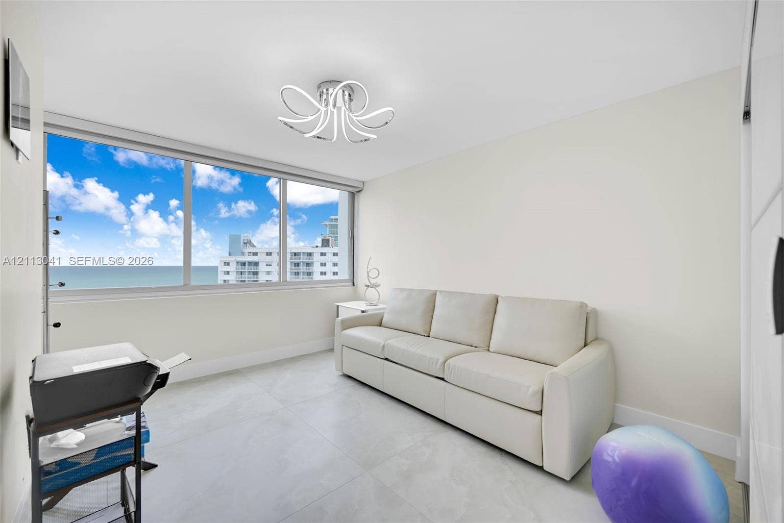 7135 Collins Avenue, #1426, Miami Beach, FL 33141 Large-format window featuring expansive coastal scenery, oversized light-colored floor tiles, and a contemporary multi-arm LED light fixture