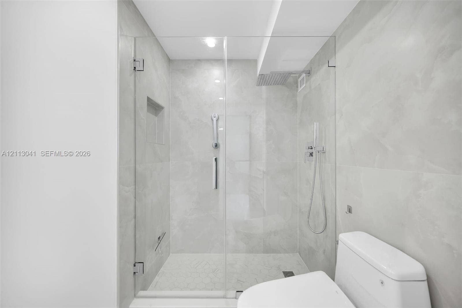 7135 Collins Avenue, #1426, Miami Beach, FL 33141 Walk-in shower featuring a frameless glass enclosure, floor-to-ceiling large-format tile surround, integrated shower niche, and wall-mounted shower system