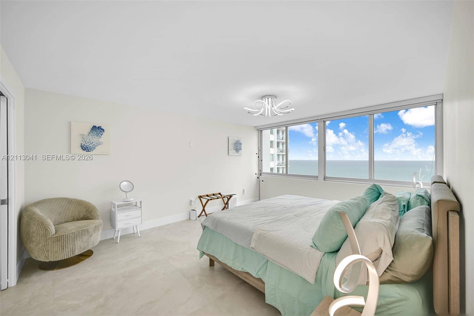 7135 Collins Avenue, #1426, Miami Beach, FL 33141 Expansive bedroom featuring large-format tile flooring, floor-to-ceiling windows with ocean and coastal scenery, and a contemporary multi-arm flush-mount light fixture