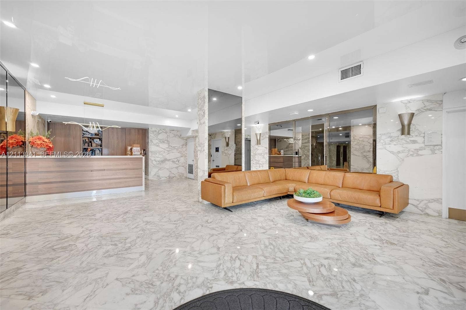 7135 Collins Avenue, #1426, Miami Beach, FL 33141 Lobby featuring large-format stone flooring, floor-to-ceiling mirrored walls, stone-clad accent pillars, integrated recessed lighting, and built-in wood-finish reception cabinetry