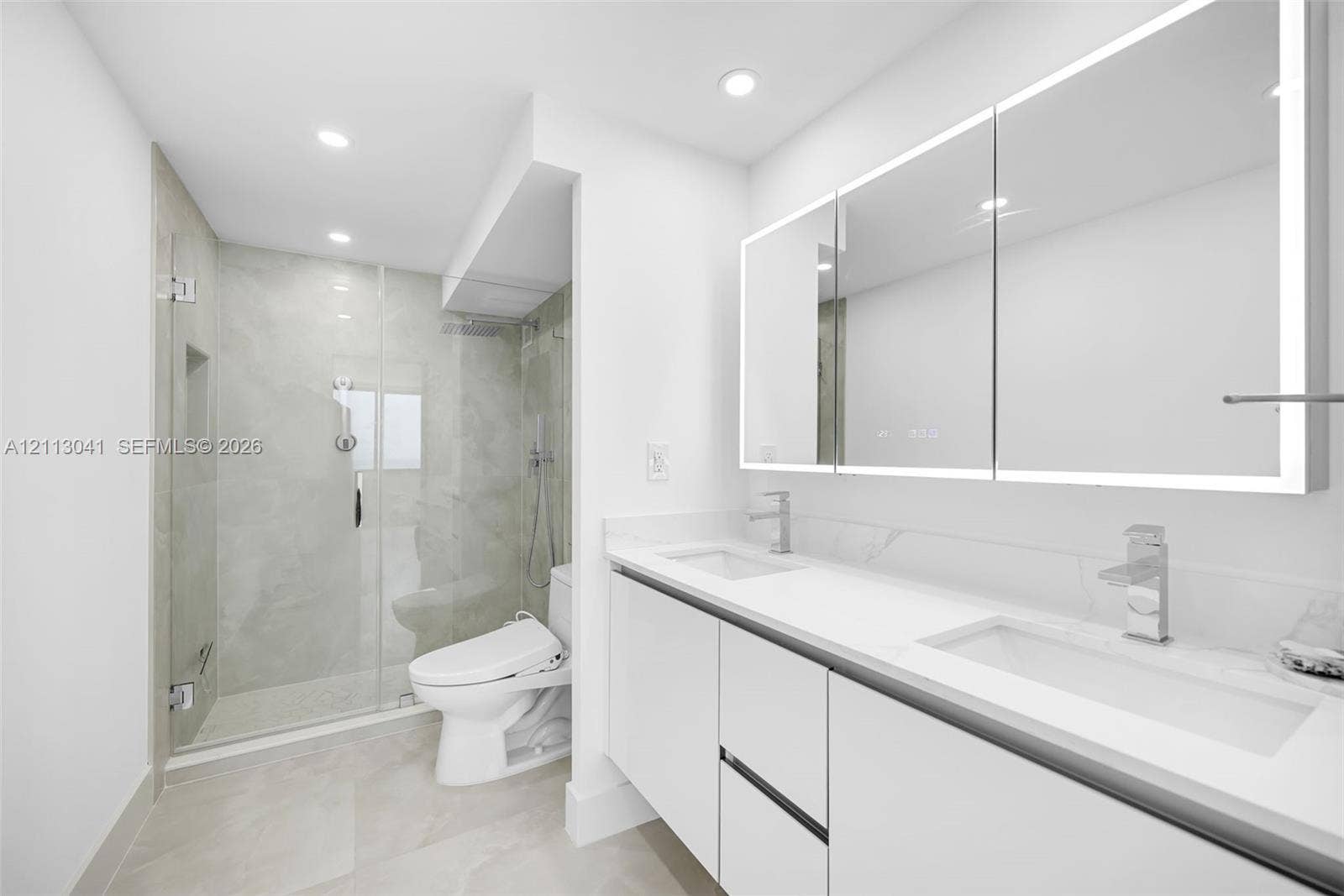 7135 Collins Avenue, #1426, Miami Beach, FL 33141 Bathroom featuring a floating double vanity with a stone countertop, integrated LED-lit medicine cabinets, a glass-enclosed walk-in shower with a rainfall showerhead, and tile flooring