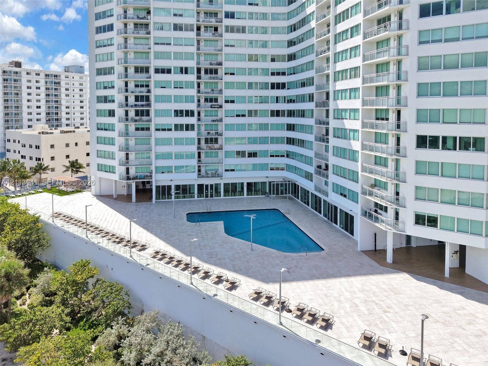 7135 Collins Avenue, #1426, Miami Beach, FL 33141 High-rise exterior featuring a paved pool deck, custom-shaped swimming pool, glass balcony railings, and exterior accent lighting