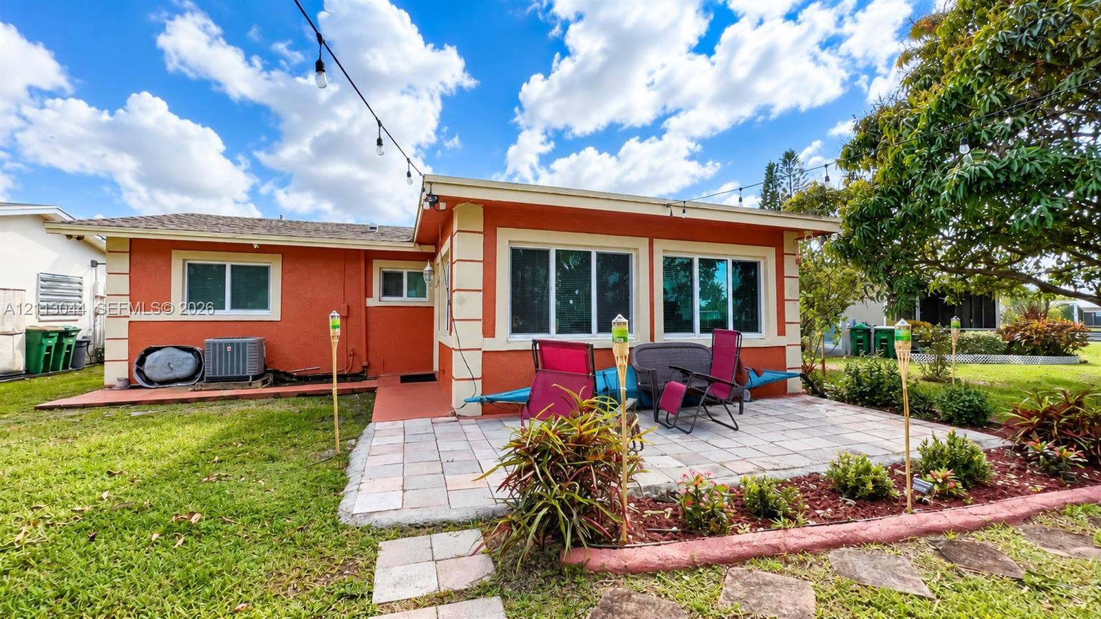 6735 NW 62nd Street, Tamarac, FL 33321 Rear exterior featuring a stucco facade with decorative corner quoins, a paved stone patio, dual-pane windows, and manicured lawn landscaping