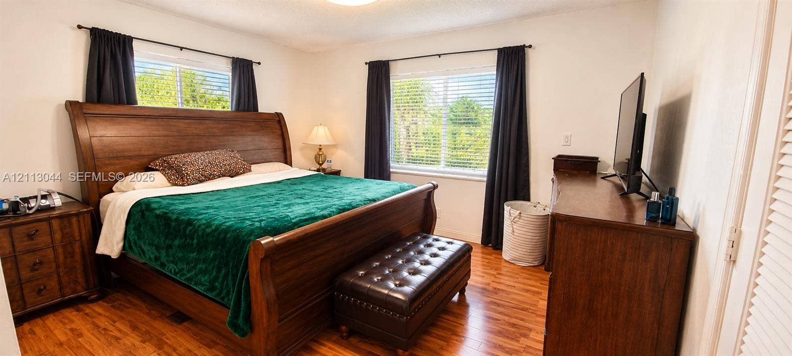 6735 NW 62nd Street, Tamarac, FL 33321 Bedroom featuring wood-finish flooring, dual windows with horizontal blinds, and louvered closet doors
