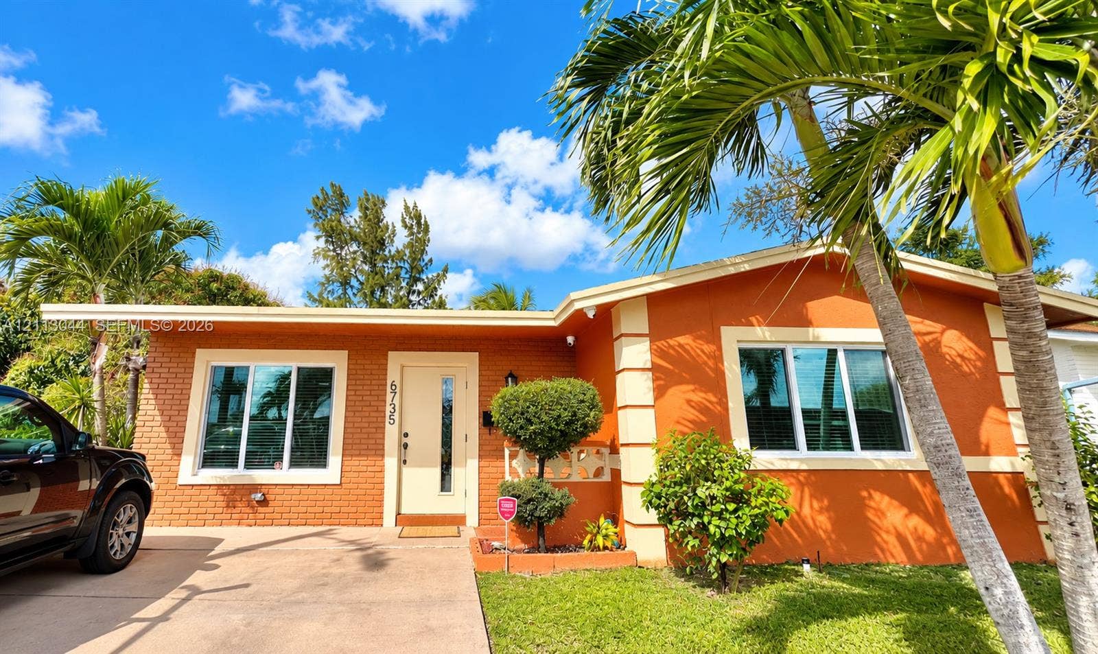 6735 NW 62nd Street, Tamarac, FL 33321 Single-story residence featuring a brick exterior, prominent quoins, an entry door with an integrated vertical window, and an attached concrete driveway
