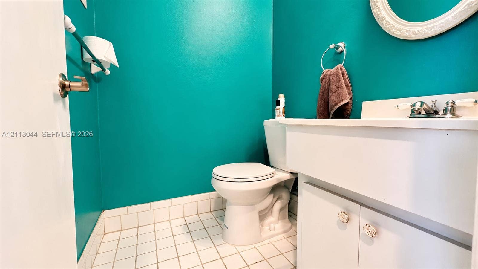6735 NW 62nd Street, Tamarac, FL 33321 Bathroom featuring white cabinetry, an integrated sink with polished chrome hardware, a wall-mounted oval mirror, and tiled flooring