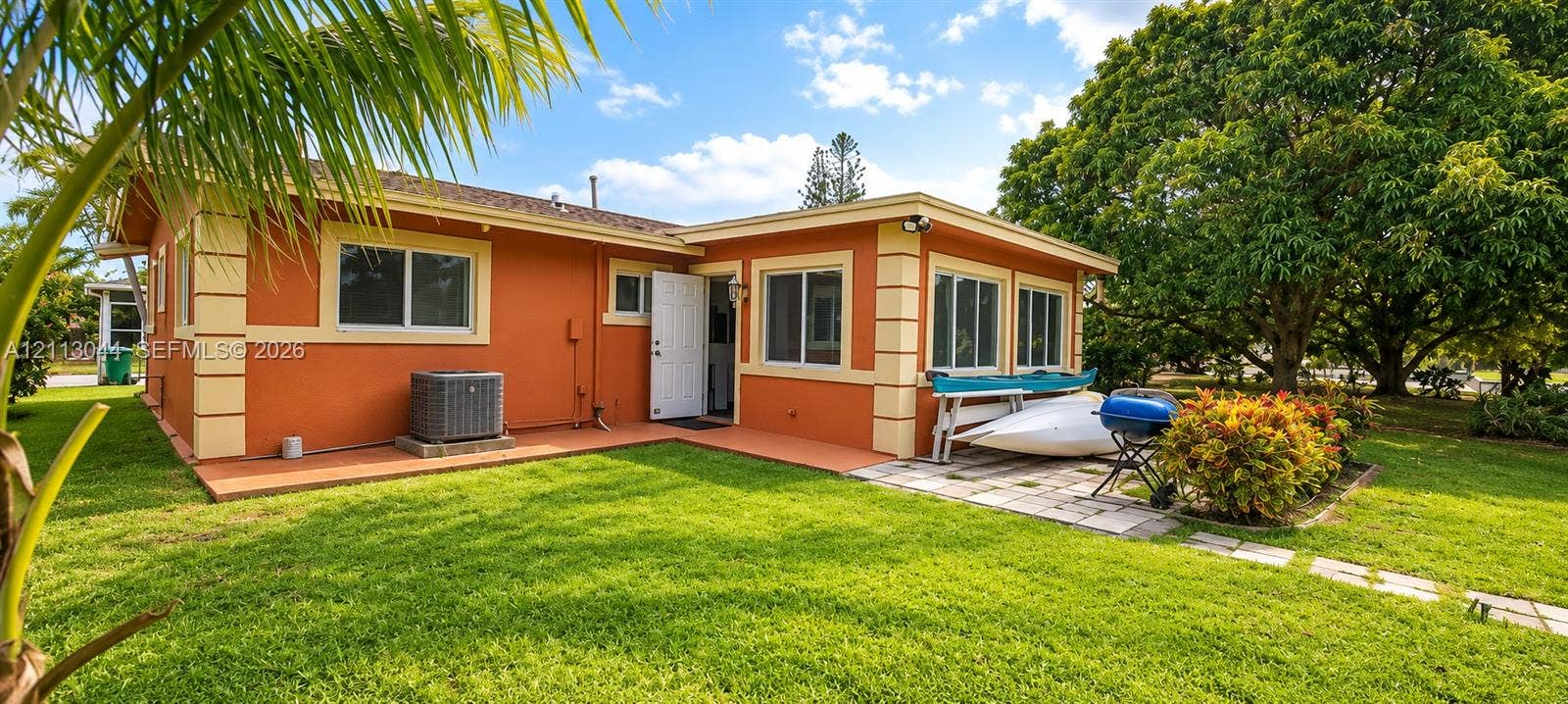 6735 NW 62nd Street, Tamarac, FL 33321 Exterior featuring stucco siding, stone corner accents, multi-pane windows, a concrete patio, and a landscaped lawn