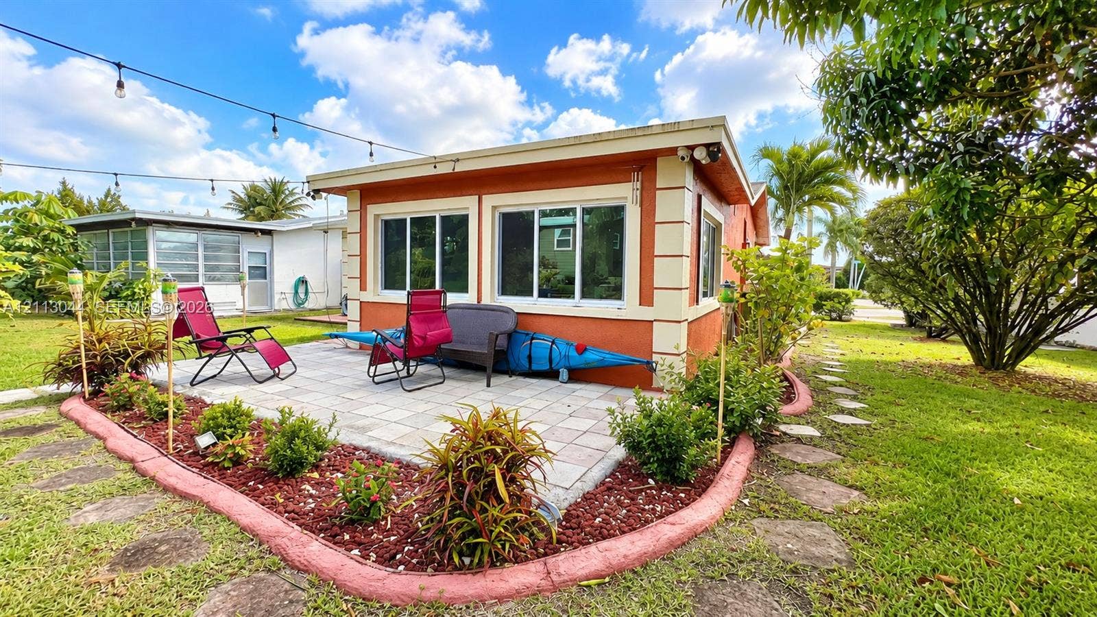 6735 NW 62nd Street, Tamarac, FL 33321 Exterior patio featuring paver flooring, landscaped garden beds with decorative borders, and string lighting