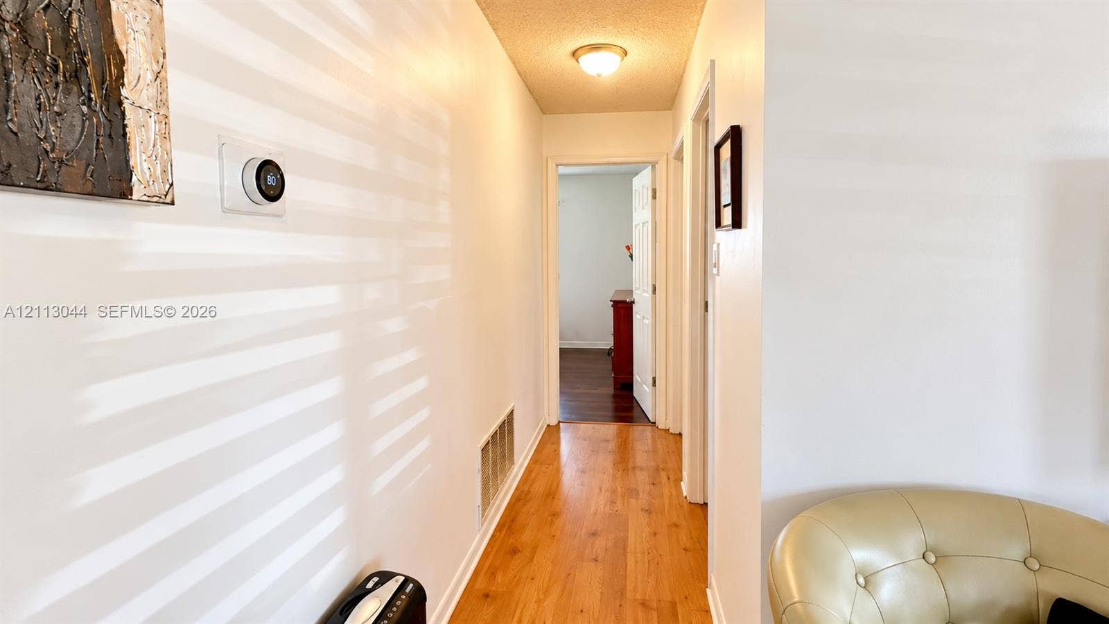 6735 NW 62nd Street, Tamarac, FL 33321 Hallway featuring wood-finish flooring, white walls, flush-mount ceiling lighting, and a smart thermostat