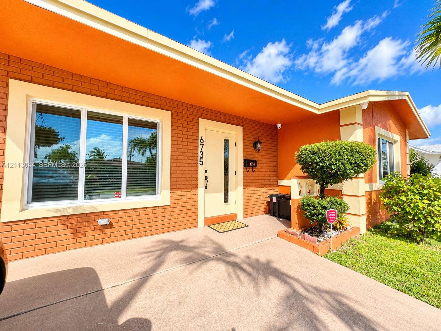 6735 NW 62nd Street, Tamarac, FL 33321 Mid-century inspired exterior featuring a brick facade, wide roof overhangs, custom trim detailing, a multi-pane front window, and a modern entry door with an integrated vertical glass panel