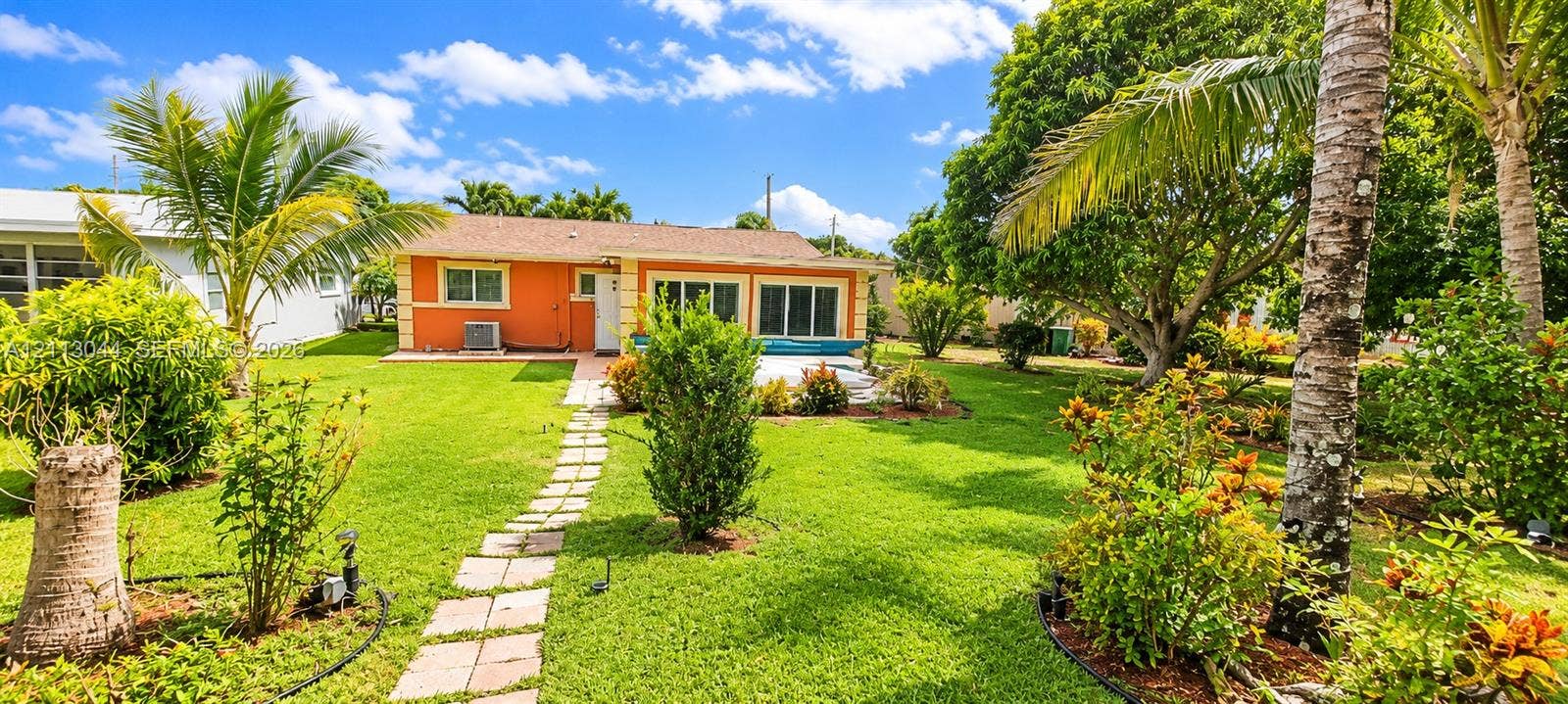 6735 NW 62nd Street, Tamarac, FL 33321 Single-story residence featuring a stucco exterior, shingled roof, stone-paver walkway, expansive lawn, and established tropical landscaping