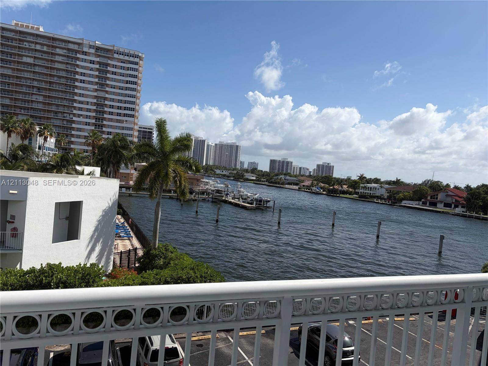 1913 S Ocean Drive, #227, Hallandale Beach, Hallandale Beach, FL 33009 Exterior balcony featuring a decorative metal railing overlooking a waterway, mature palm trees, and coastal urban scenery