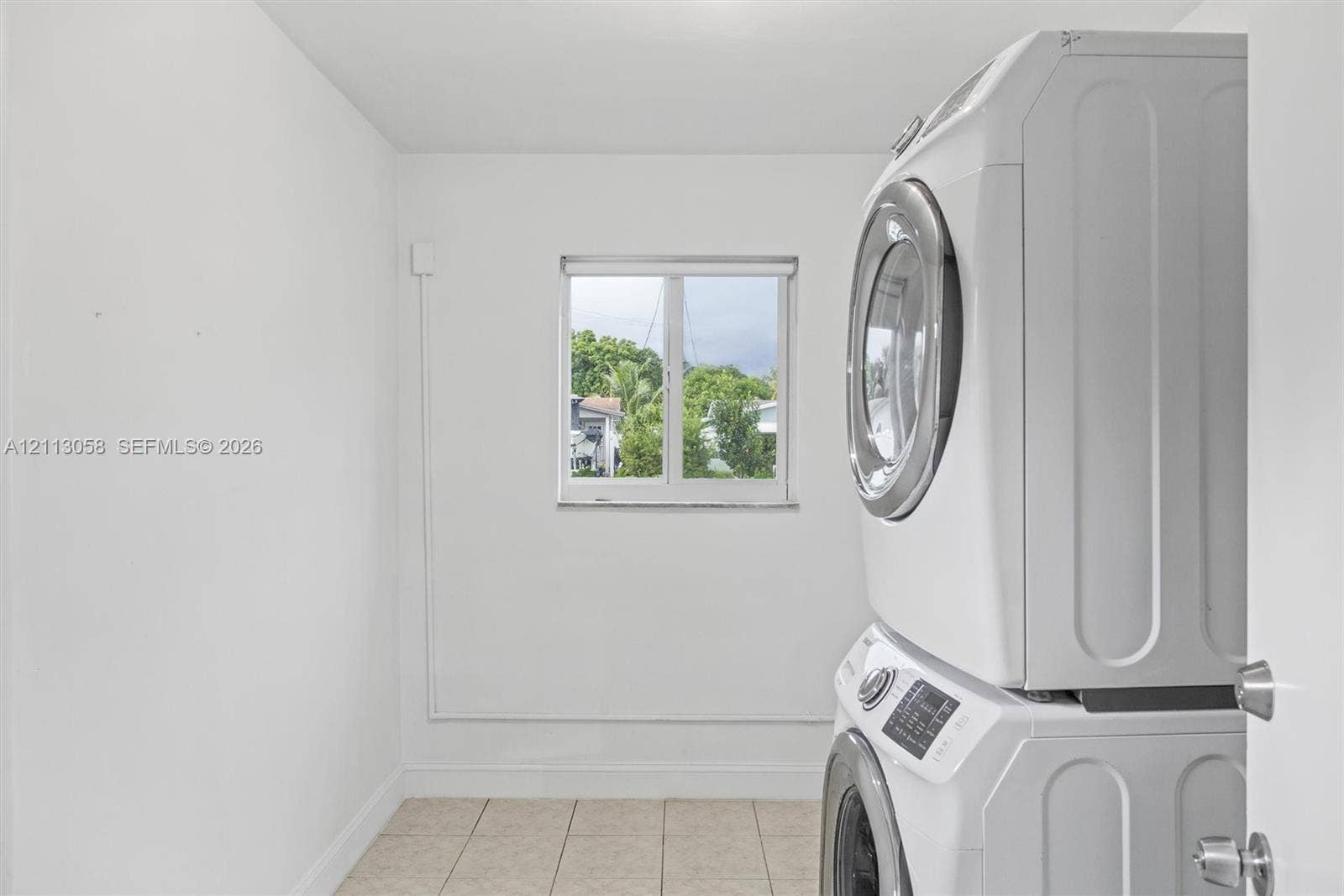1980 NW 33rd Court, Oakland Park, FL 33309 Utility area featuring a stacked washer and dryer unit, neutral ceramic tile flooring, and a window providing natural light