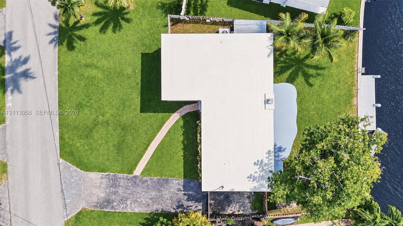 1980 NW 33rd Court, Oakland Park, FL 33309 Aerial perspective of a waterfront lot featuring a private dock, asphalt driveway, meandering paved walkway, and landscaped lawn with mature trees