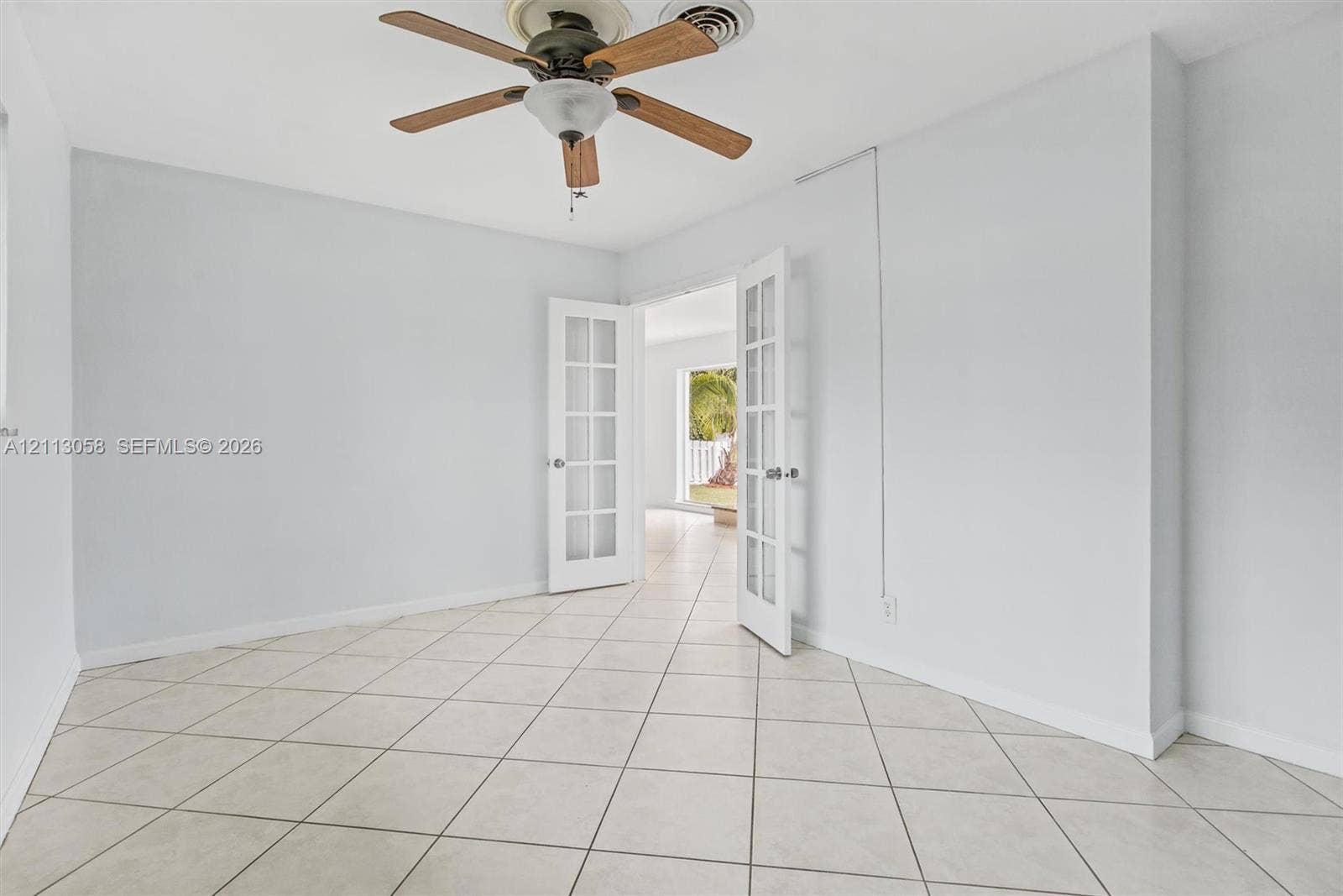 1980 NW 33rd Court, Oakland Park, FL 33309 Interior space featuring large-format diagonal tile flooring, white French doors with glass panes, and a ceiling-mounted fan with wood-finish blades