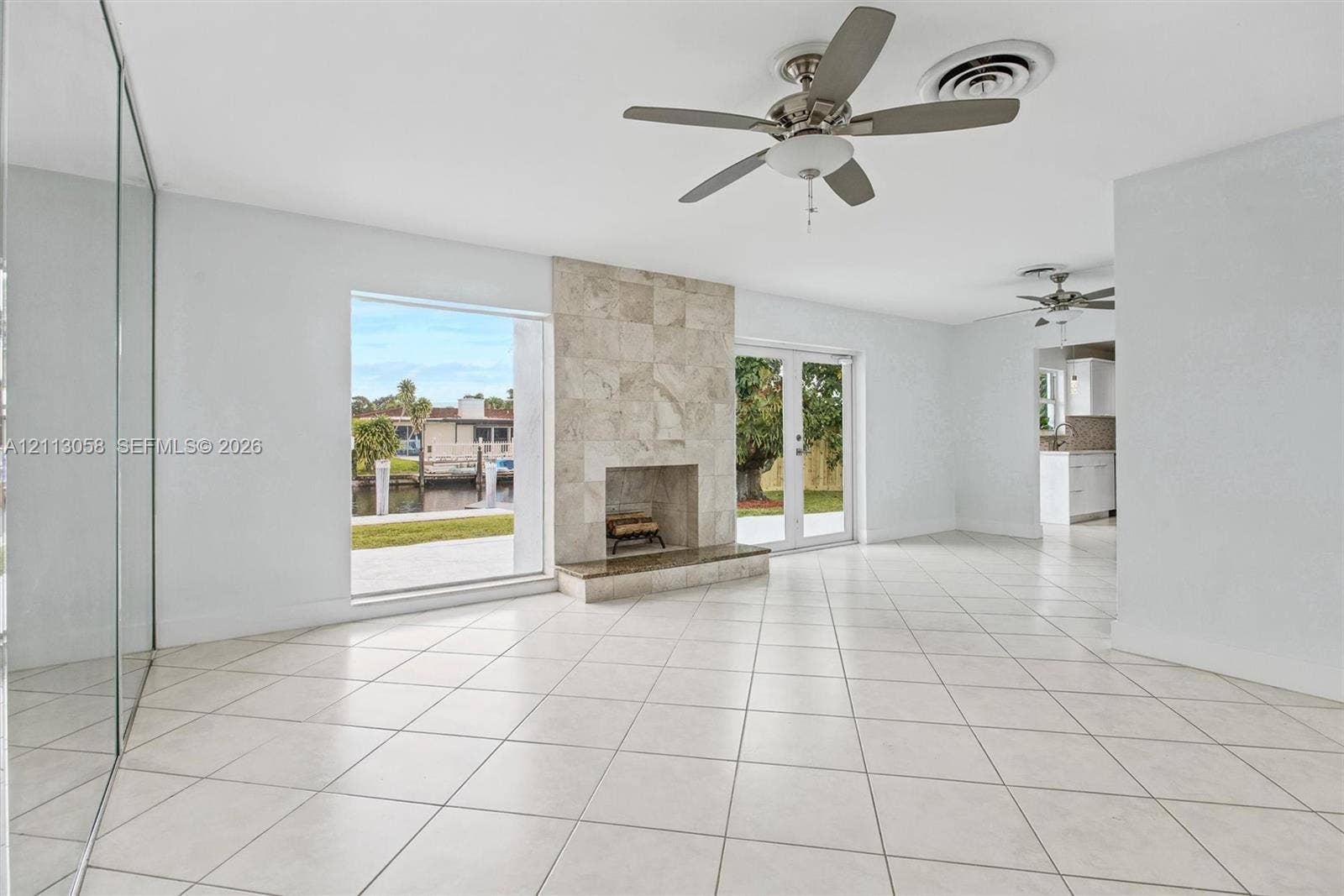 1980 NW 33rd Court, Oakland Park, FL 33309 Living area featuring tile flooring, a floor-to-ceiling stone-tiled fireplace, dual ceiling fans, a large picture window, and glass-paned double doors