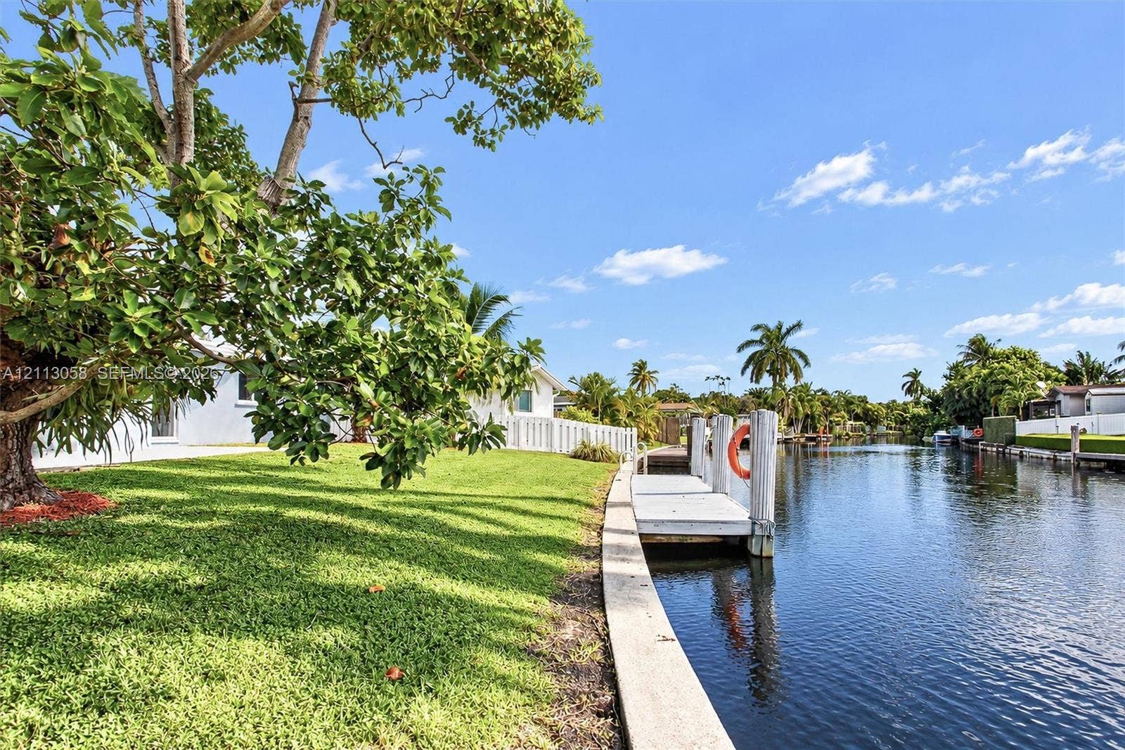 1980 NW 33rd Court, Oakland Park, FL 33309 Canal-front property featuring a private dock, concrete seawall, mature landscaping, and an expansive lawn