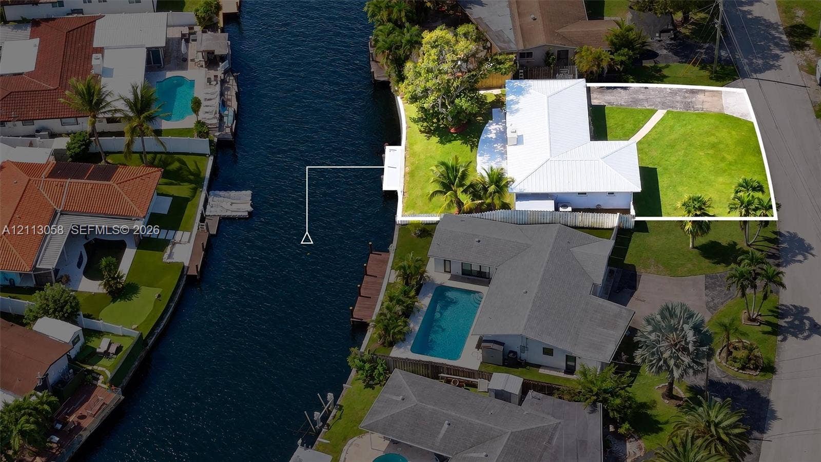 1980 NW 33rd Court, Oakland Park, FL 33309 Waterfront property featuring a private dock, expansive lawn, paved driveway, and mature landscaping