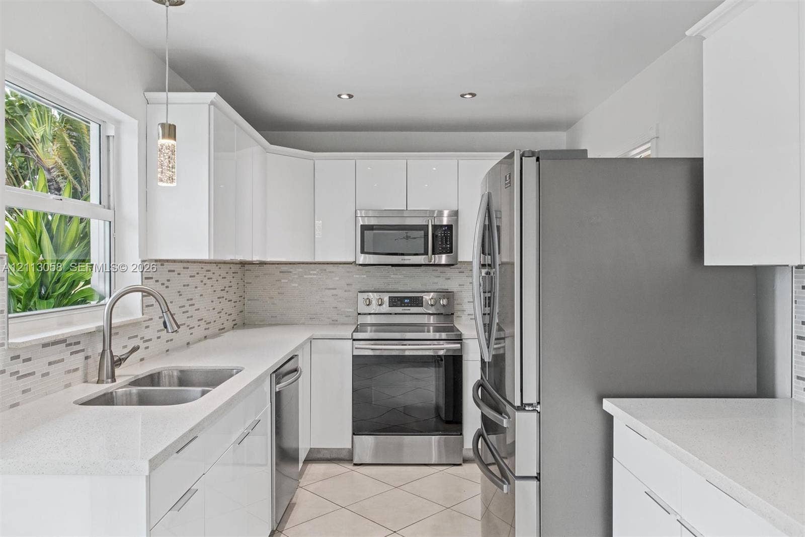 1980 NW 33rd Court, Oakland Park, FL 33309 Kitchen featuring white gloss cabinetry, quartz countertops, stainless steel appliances, a mosaic tile backsplash, and ceramic tile flooring
