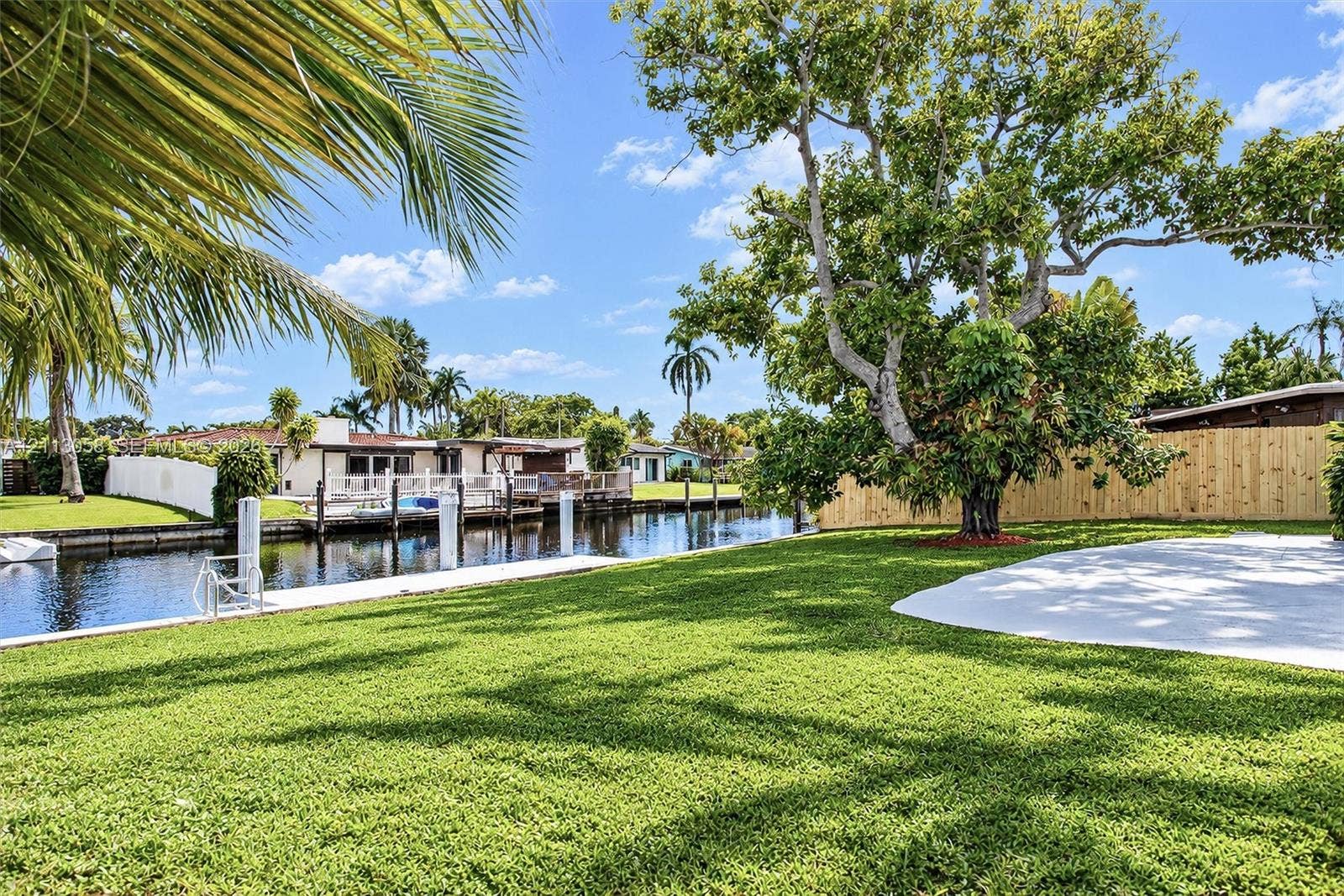 1980 NW 33rd Court, Oakland Park, FL 33309 Waterfront backyard featuring a concrete dock, private canal bulkhead, mature trees, and a paved patio area