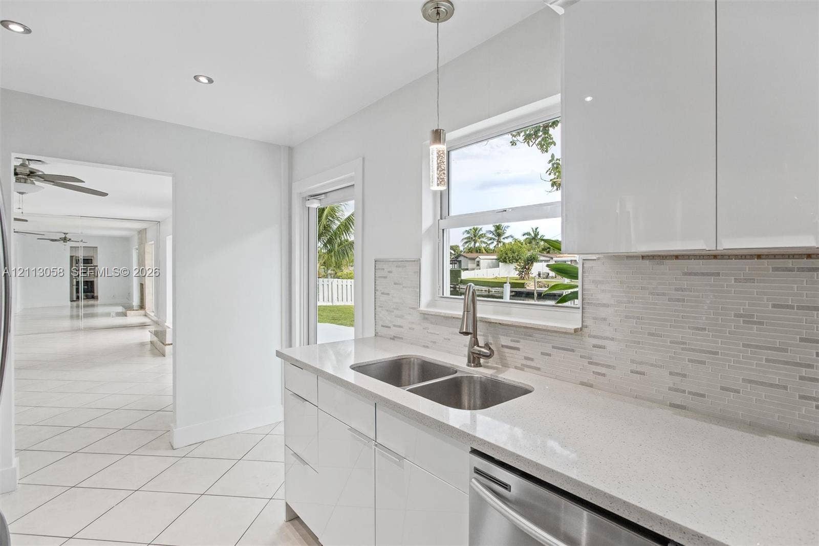 1980 NW 33rd Court, Oakland Park, FL 33309 Kitchen featuring high-gloss white cabinetry, quartz countertops, a stone-pattern tile backsplash, stainless steel dual-basin sink with a pull-down faucet, and recessed lighting