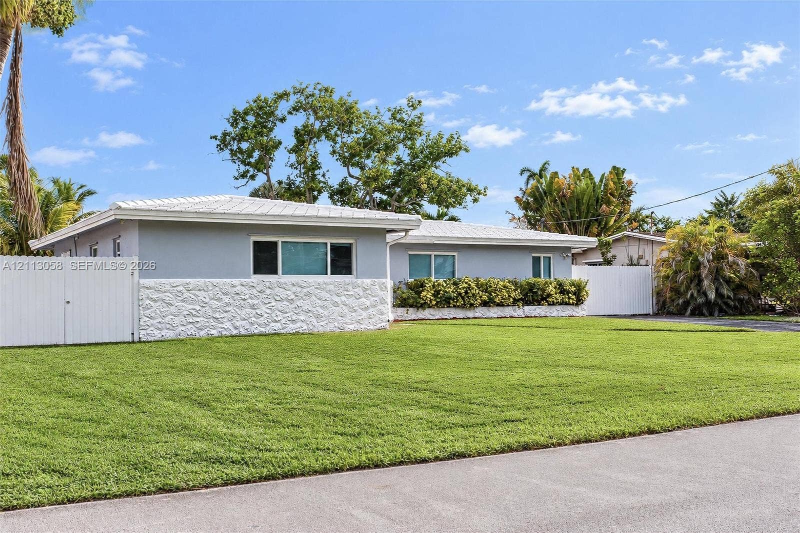 1980 NW 33rd Court, Oakland Park, FL 33309 Single-story residence featuring a textured masonry facade, light-toned exterior finish, metal roofing, and privacy fencing enclosing the perimeter