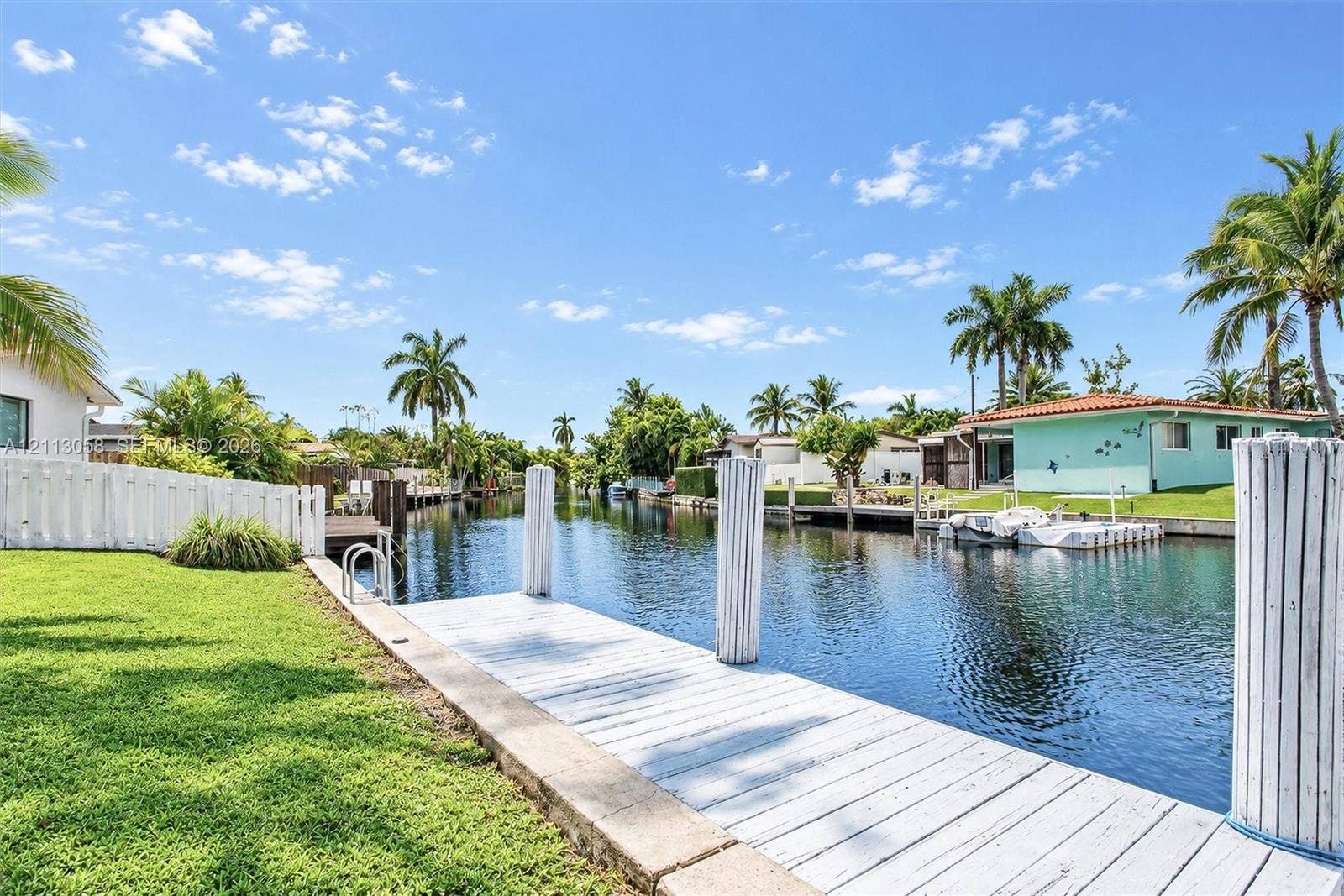 1980 NW 33rd Court, Oakland Park, FL 33309 Waterfront property featuring a private white-painted wooden dock, bulkhead sea wall, manicured lawn, and perimeter fencing