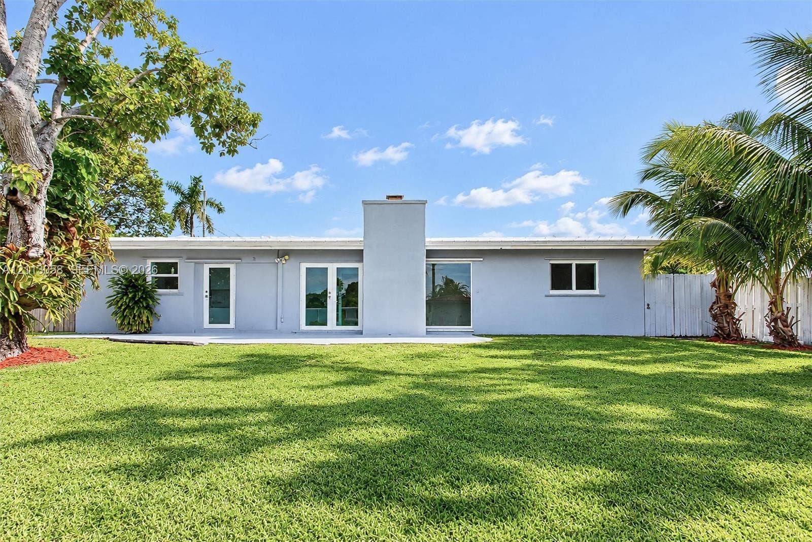 1980 NW 33rd Court, Oakland Park, FL 33309 Single-story exterior featuring a concrete patio, exterior masonry chimney, dual glass panel entry doors, and mature landscaping