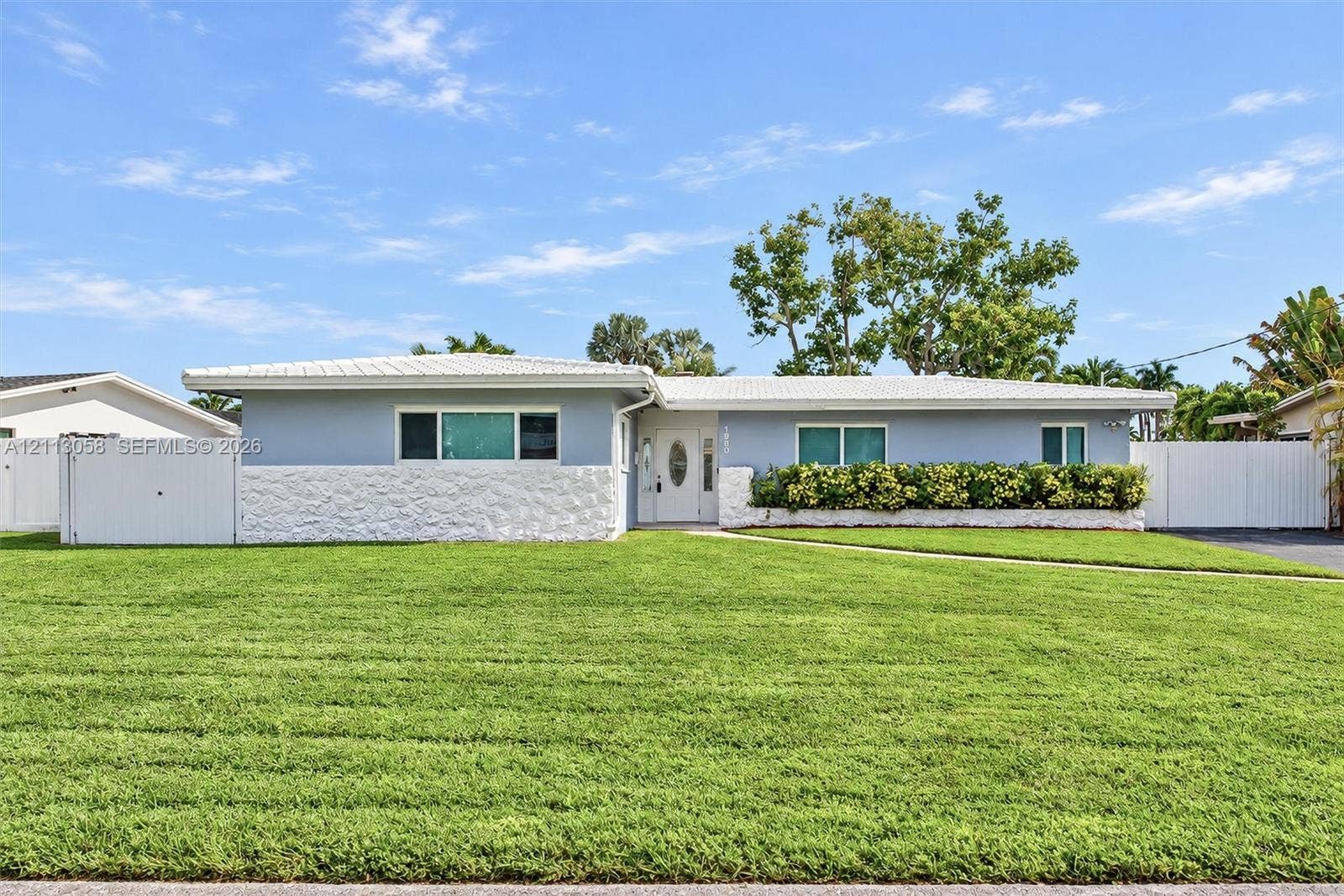 1980 NW 33rd Court, Oakland Park, FL 33309 Single-story exterior featuring light-toned masonry, textured stone wainscoting, a covered entry with an oval-glass door, and vinyl perimeter fencing