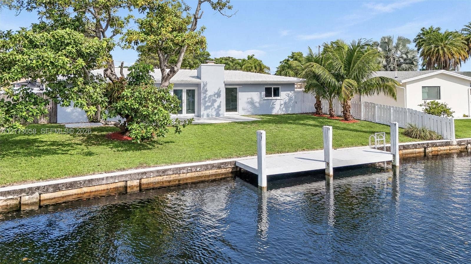 1980 NW 33rd Court, Oakland Park, FL 33309 Waterfront residence featuring a private boat dock, concrete seawall, expansive lawn, and white vinyl perimeter fencing