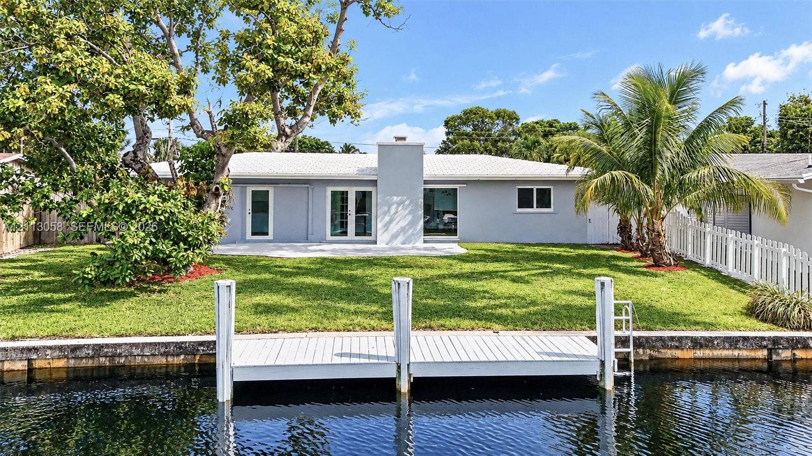 1980 NW 33rd Court, Oakland Park, FL 33309 Waterfront property featuring a private dock, expansive lawn, exterior chimney, and white picket fencing