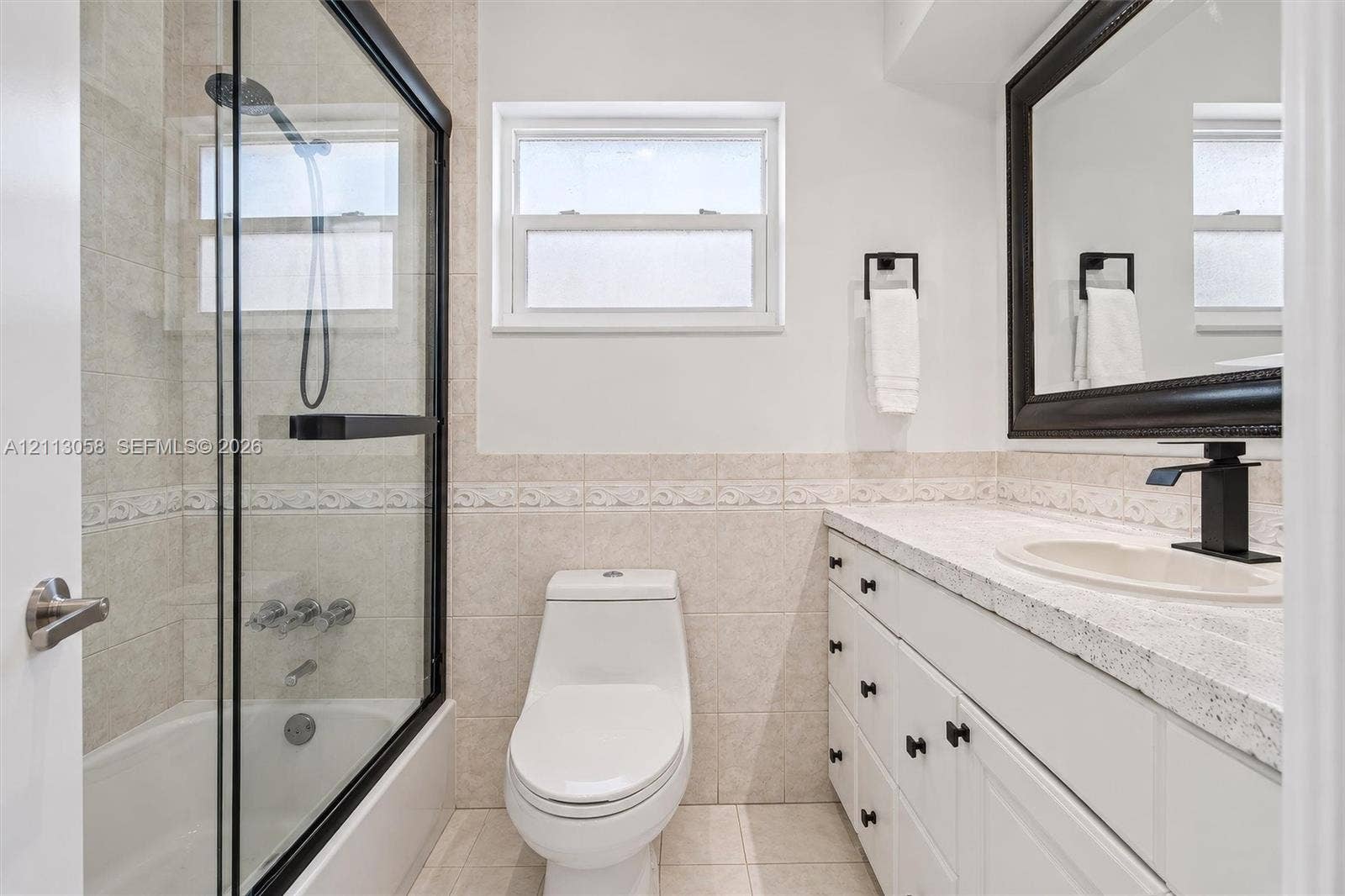 1980 NW 33rd Court, Oakland Park, FL 33309 Bathroom featuring a shower-tub combination with a black-framed glass enclosure, vanity with speckled countertop and integrated basin, matte black faucet hardware, and neutral tile wall accents