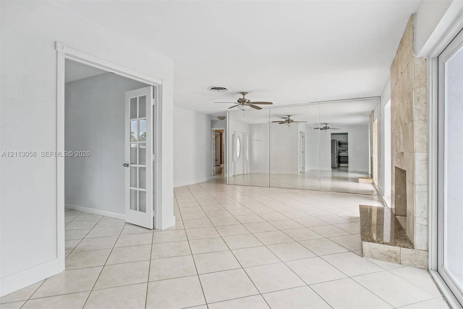 1980 NW 33rd Court, Oakland Park, FL 33309 Neutral-toned tile flooring, floor-to-ceiling mirrored wall paneling, fireplace featuring a stone-tile hearth, and glass-paned French doors