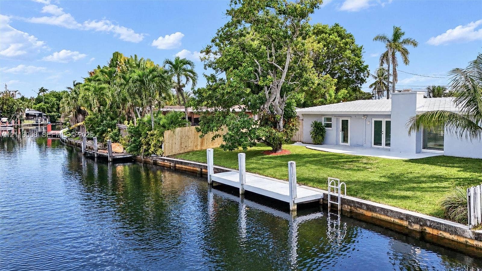 1980 NW 33rd Court, Oakland Park, FL 33309 Waterfront property featuring a private dock, concrete seawall, expansive lawn, mature palm trees, and a ground-level patio