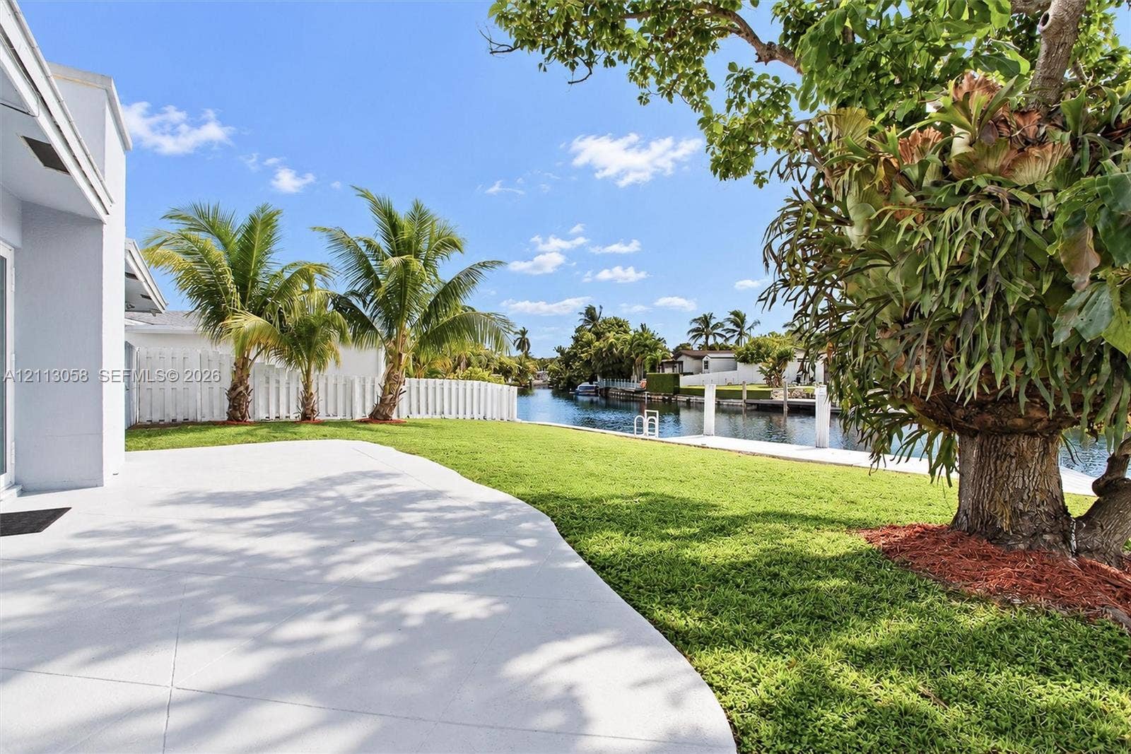 1980 NW 33rd Court, Oakland Park, FL 33309 Waterfront backyard featuring a concrete patio, a manicured lawn, palm trees, and a private dock