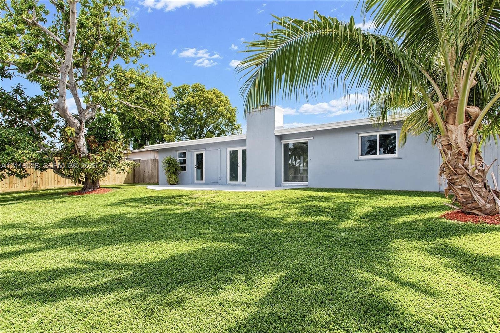 1980 NW 33rd Court, Oakland Park, FL 33309 Expansive rear yard featuring a manicured lawn, concrete patio, exterior chimney, and mature trees