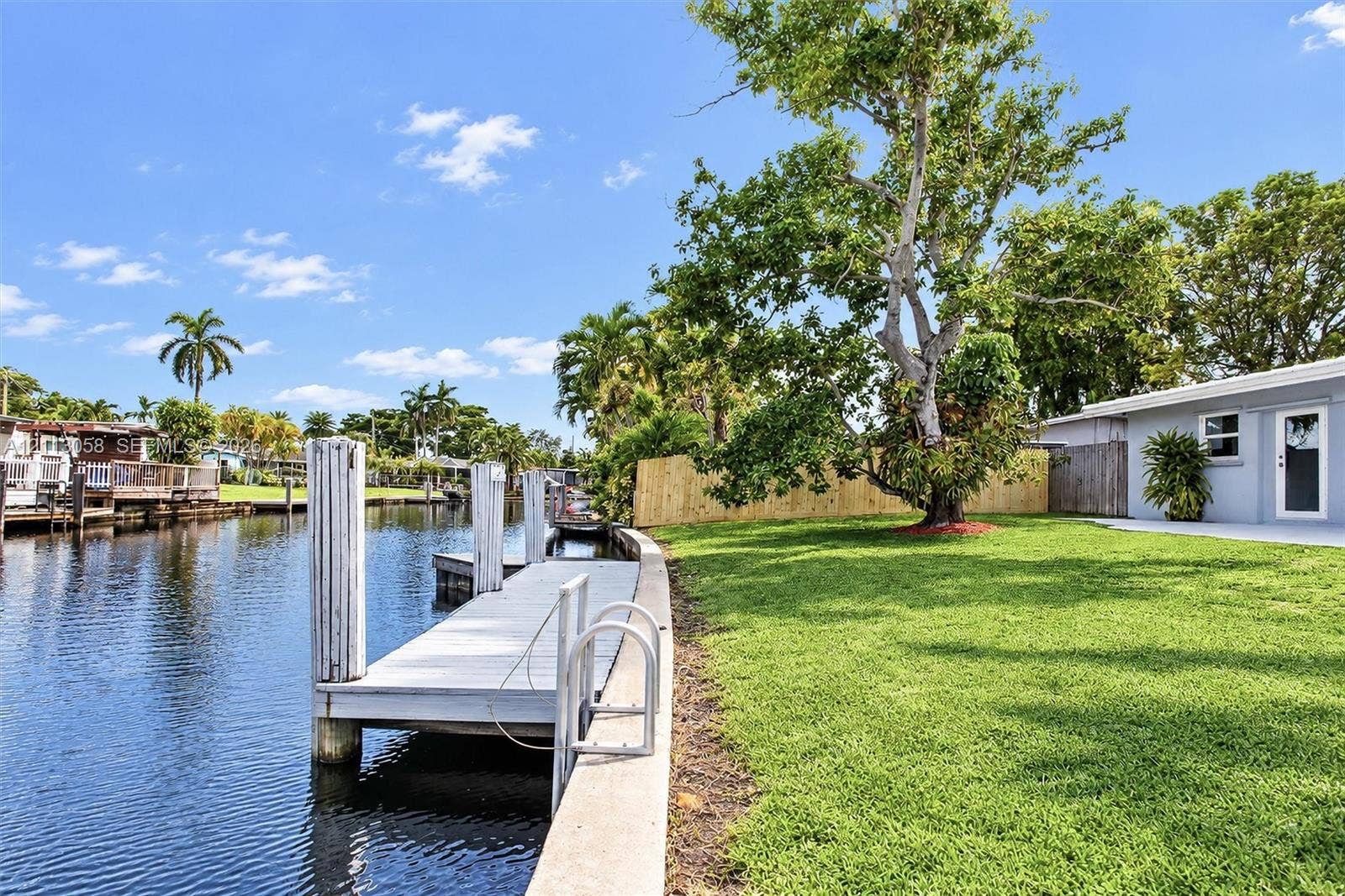 1980 NW 33rd Court, Oakland Park, FL 33309 Waterfront backyard featuring a private dock, concrete seawall, manicured lawn, and mature trees