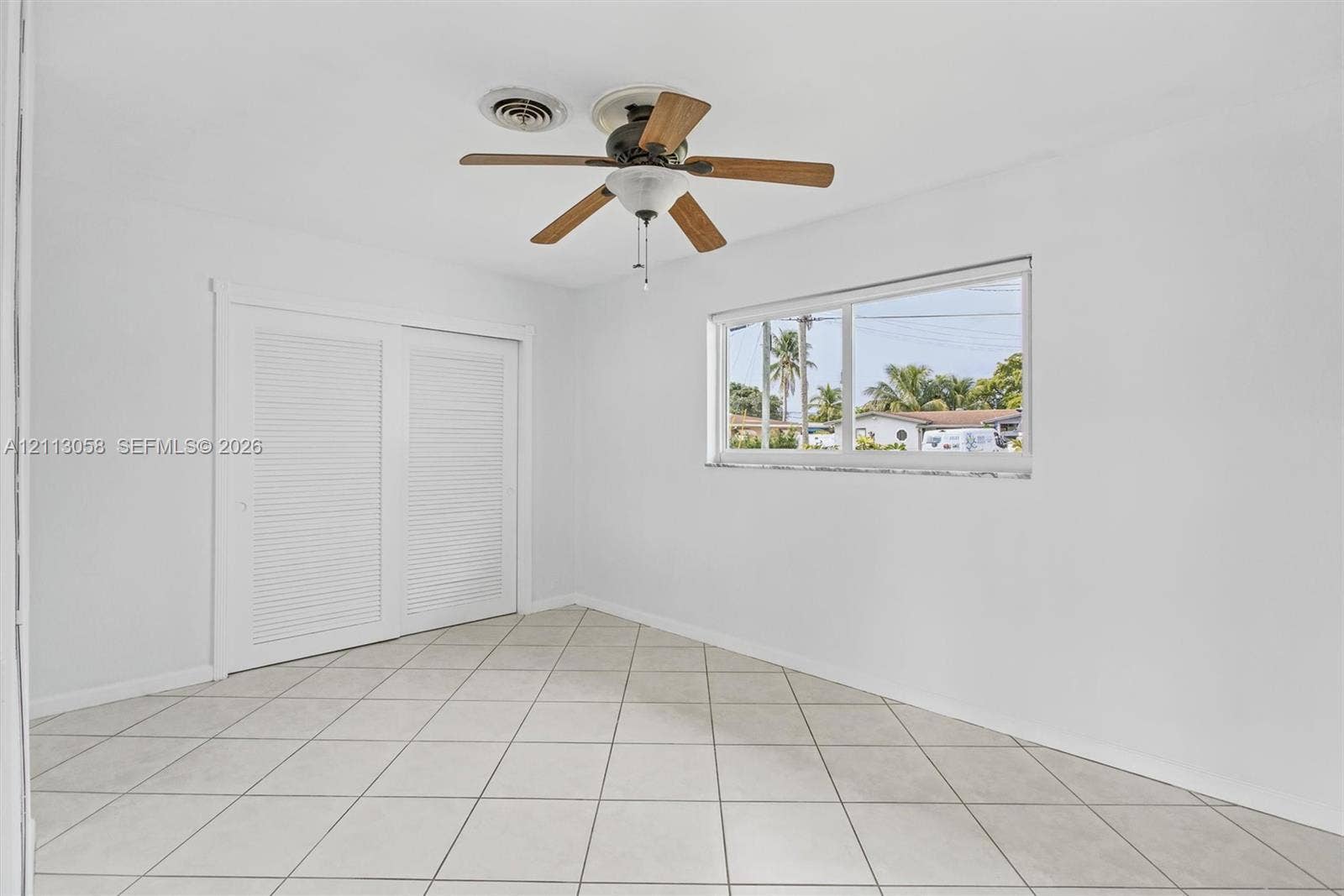 1980 NW 33rd Court, Oakland Park, FL 33309 Interior space featuring neutral tile flooring, louvered closet doors, and a ceiling fan with integrated lighting