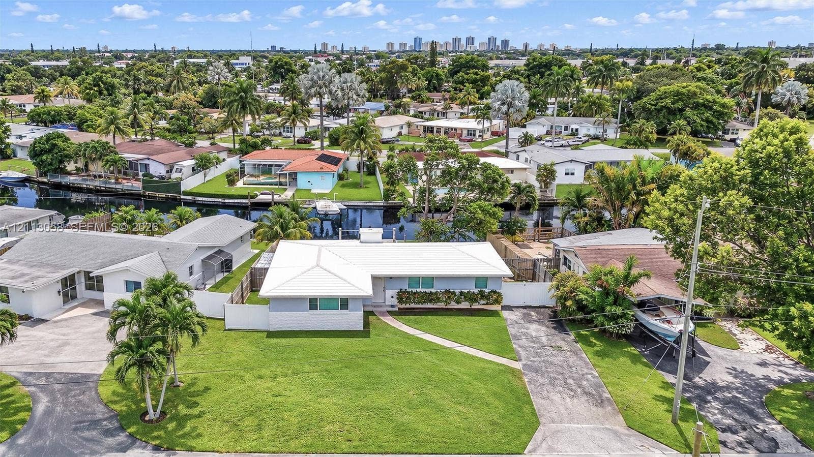 1980 NW 33rd Court, Oakland Park, FL 33309 Single-story residence featuring a metal roof, attached asphalt driveway, manicured lawn, and water frontage with a bulkhead