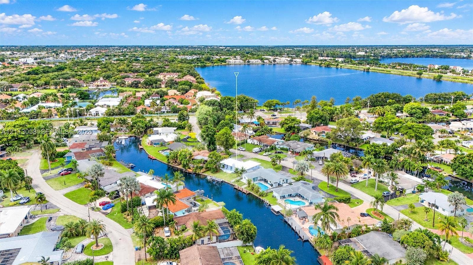 1980 NW 33rd Court, Oakland Park, FL 33309 Aerial view of waterfront property featuring canal access, private swimming pool, light-colored roof, and proximity to expansive lake