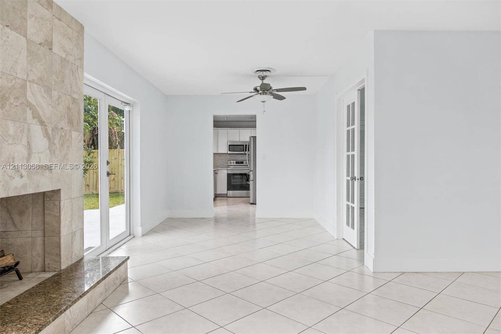 1980 NW 33rd Court, Oakland Park, FL 33309 Stone-clad fireplace with a polished hearth, ceramic tile flooring set on a diagonal, French doors with glass panes, and a ceiling fan