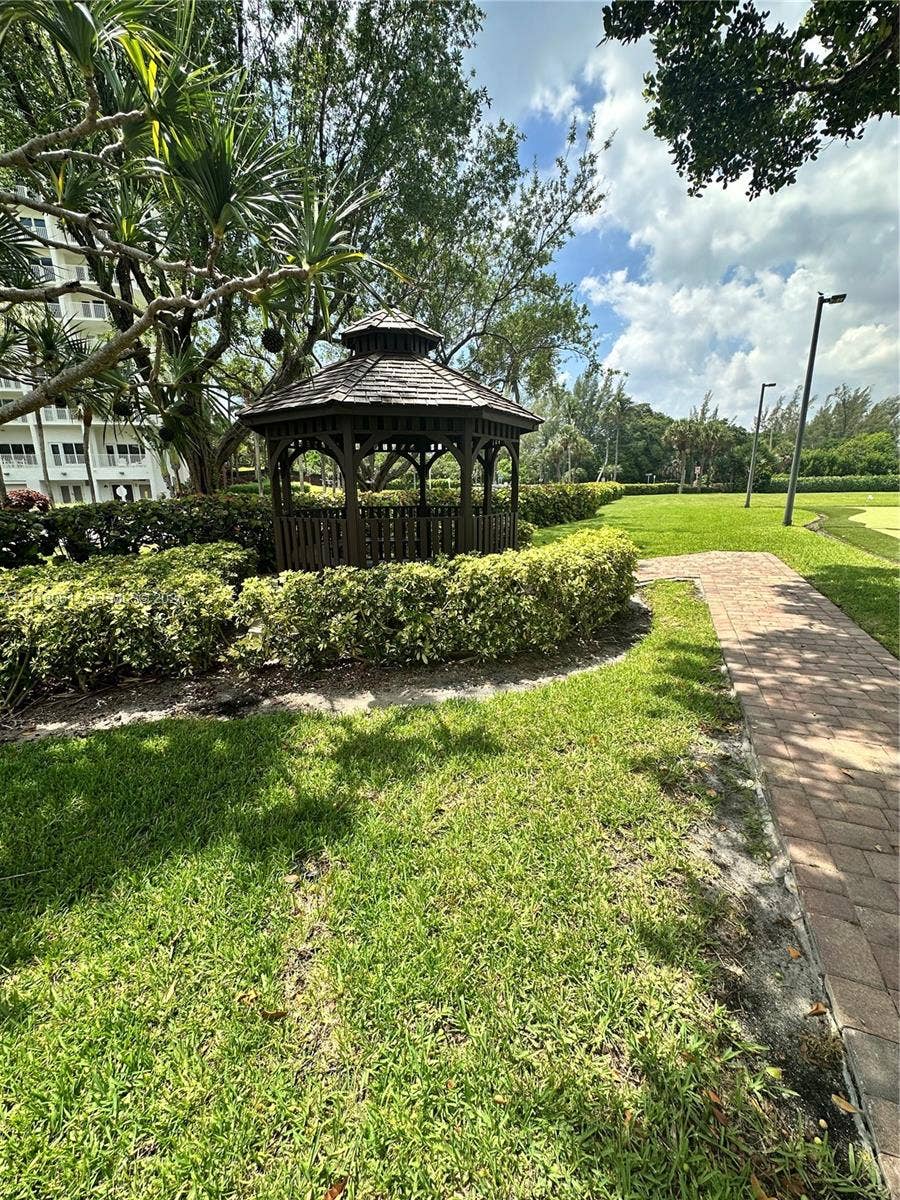 Outdoor gazebo featuring a tiered roof and dark wood structure, situated among mature landscaping with a paved walkway