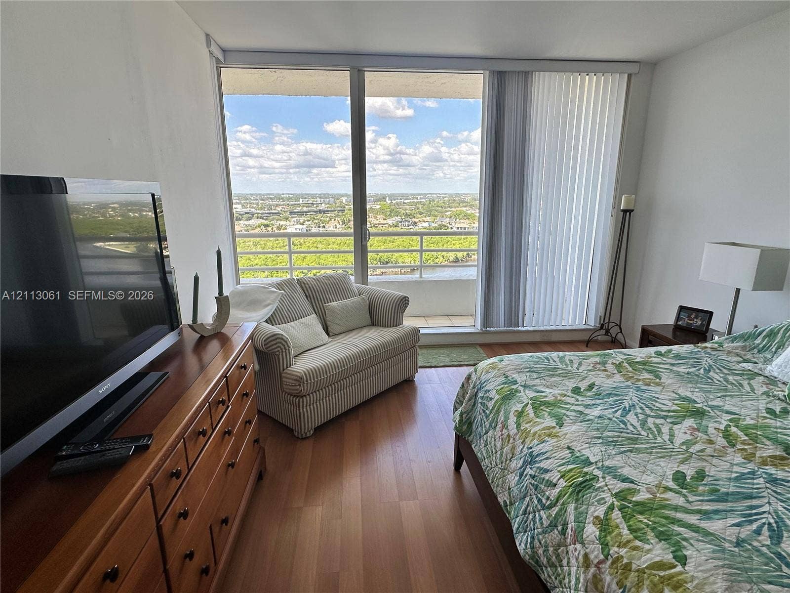 Floor-to-ceiling glass sliding doors with vertical blinds, private balcony, and wood-finish flooring