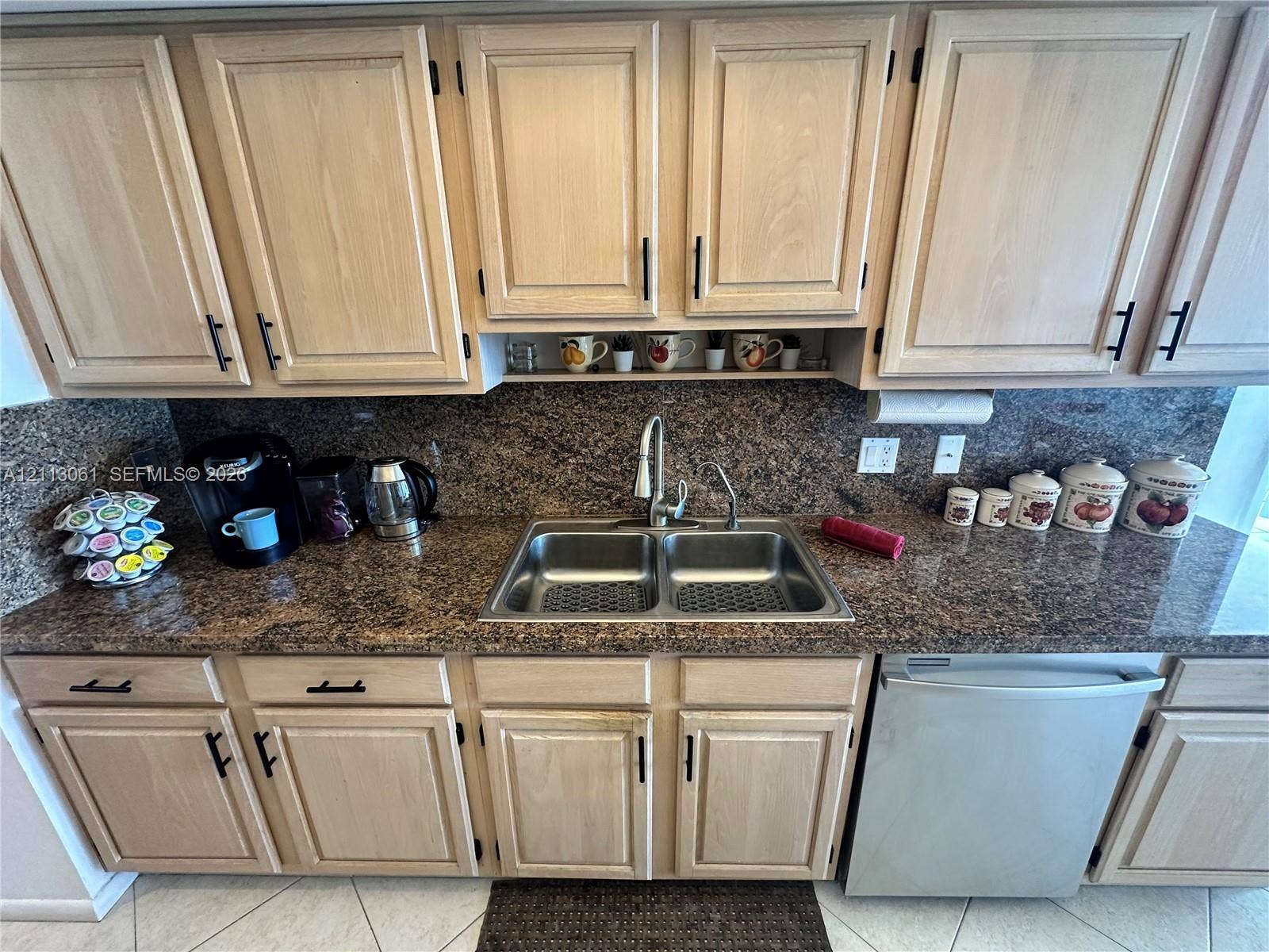 Light-toned wood cabinetry with matte black hardware, stone-finish countertops, dual-basin stainless steel sink, pull-down faucet, and integrated stainless steel dishwasher