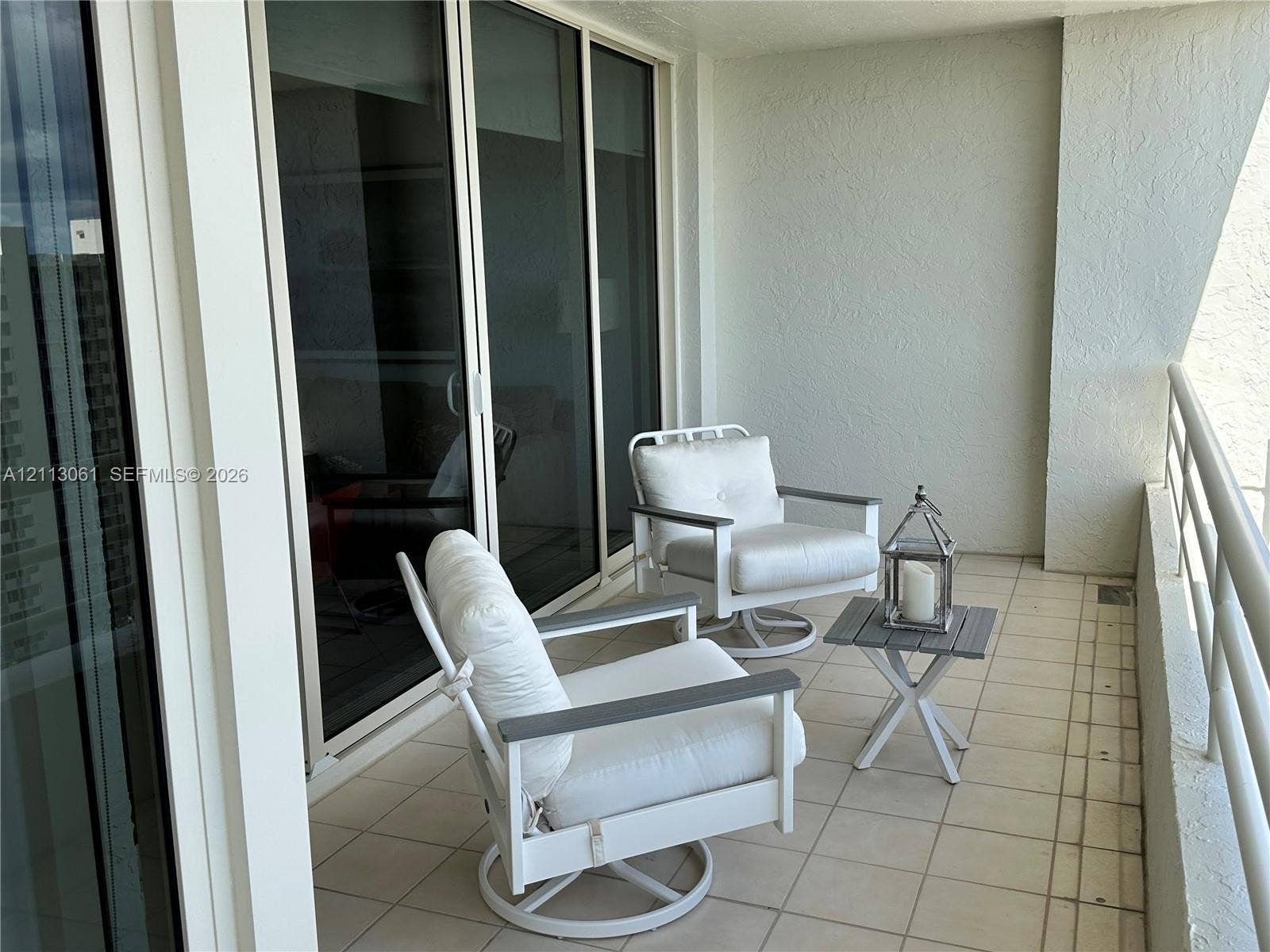 Covered balcony featuring neutral ceramic tile flooring, textured stucco walls, and floor-to-ceiling sliding glass doors with aluminum framing