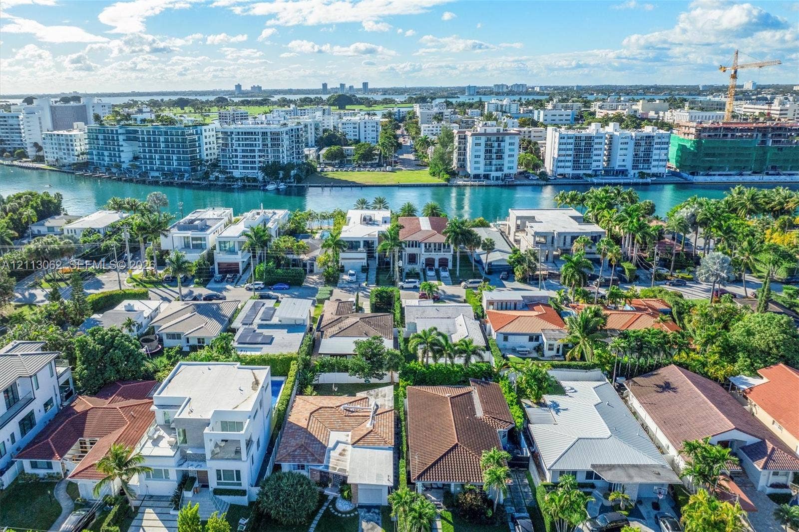 Aerial perspective of a coastal residential area featuring waterfront property, deep-water canal access, mature palm trees, and varied architectural styles