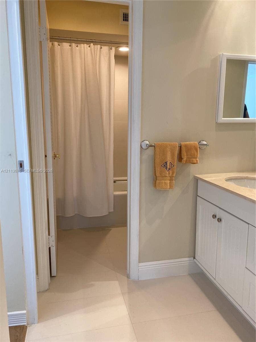 Bathroom featuring a white vanity cabinet with an integrated sink, stone-finish countertop, wall-mounted rectangular mirror, and a tiled shower area